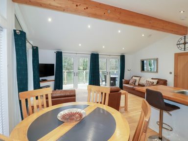 An open living room and kitchen area with a round dining table chairs brown leather sofas and glass doors with curtains at 2 Miller's Island Near Lanreath