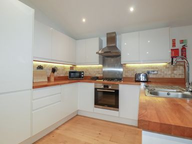 A kitchen with white cabinets wooden countertops a microwave toaster stove oven and sink at 2 Miller's Island Near Lanreath