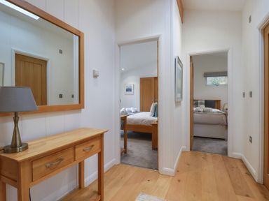 A hallway with a wooden console table and lamp facing two bedrooms with beds at 2 Miller's Island Near Lanreath