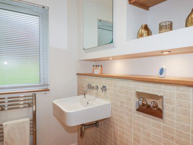 A bathroom with a wall-mounted sink towel rack window with blinds and storage shelf at 2 Miller's Island Near Lanreath
