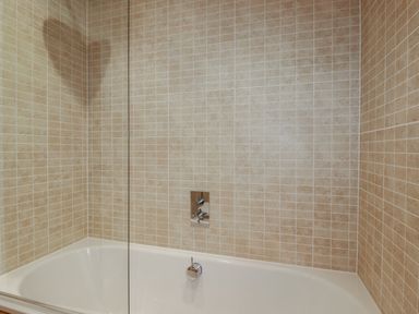 A bathtub with beige tiled walls and a glass partition at 2 Miller's Island Near Lanreath