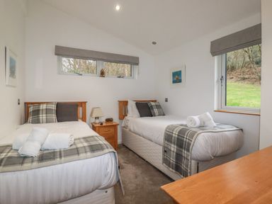 A bedroom with two single beds with plaid blankets and pillows a wooden nightstand with a lamp a window showing grass and trees at 2 Miller's Island Near Lanreath
