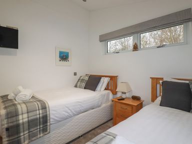 A bedroom with two single beds a wooden nightstand a lamp a wall-mounted television and a window at 2 Miller's Island Near Lanreath