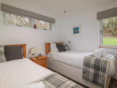 A bedroom with two single beds a wooden nightstand with a lamp and a window at 2 Miller's Island Near Lanreath