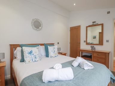 A bedroom with a bed with floral cushions and folded towels on a blue throw at 2 Miller's Island Near Lanreath