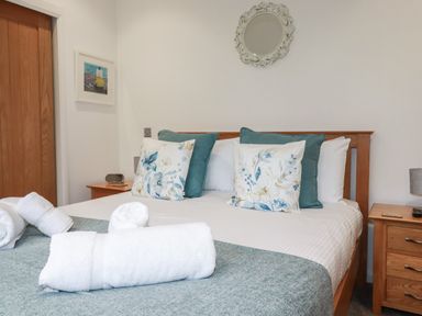 A bedroom with a wooden bed frame pillows with floral and solid covers bedside tables with lamps and rolled white towels on bed at 2 Millers Island Near Lanreath