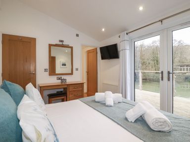 A bedroom with a bed with rolled towels a mirror and desk doors leading to an outside deck at 2 Miller's Island Near Lanreath