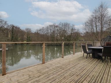 A wooden deck with a glass railing overlooking a river and trees with outdoor furniture at 2 Millers Island Near Lanreath