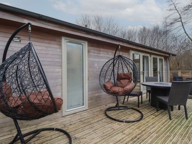An outdoor wooden deck with two hanging egg chairs and a dining table with four chairs at 2 Millers Island Near Lanreath
