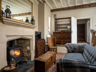 A living room with a fireplace wood stove and wooden furniture including a sofa chair and chest at Courtyard House in Blockley
