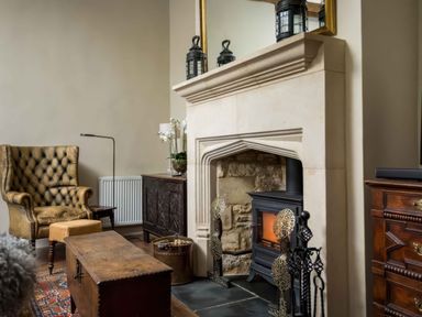 A living room with a stone fireplace a wood-burning stove an armchair and wooden furniture at Courtyard House in Blockley