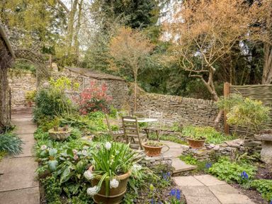 A garden with stone walls wooden chairs and a table surrounded by plants and flowers at Courtyard House in Blockley