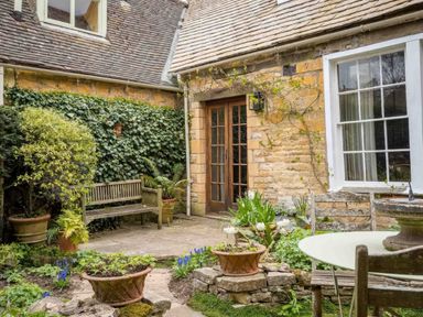 An outdoor courtyard with stone walls wooden bench potted plants and a round table with chairs at Courtyard House in Blockley