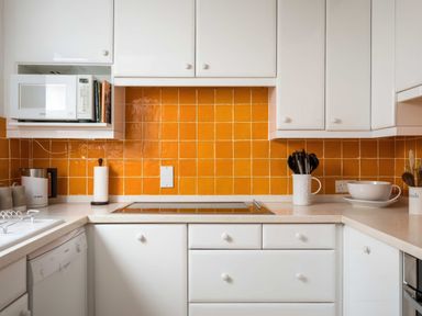 A kitchen with white cabinets and orange tiled backsplash with microwave and utensils at Courtyard House in Blockley