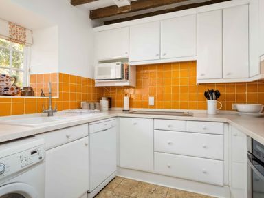 A kitchen with white cabinets orange tiled backsplash and appliances at Courtyard House in Blockley