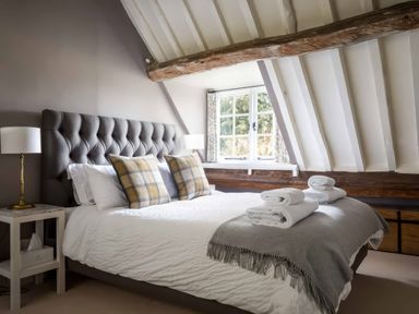A bedroom with a large bed with pillows and folded towels near a window at Courtyard House in Blockley