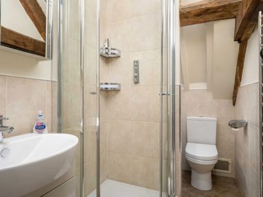 A bathroom with a shower enclosure sink with soap dispenser and a toilet under exposed wooden beams at Courtyard House Blockley