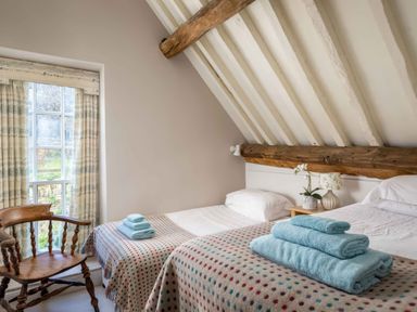 A bedroom with two single beds a wooden chair and a window with curtains at Courtyard House in Blockley