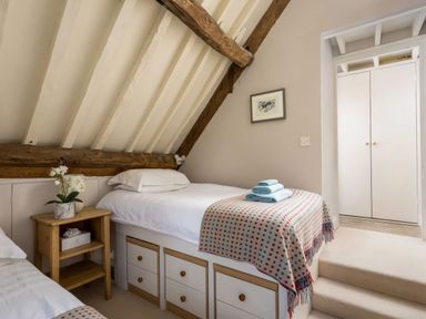 A bedroom with two beds a wooden bedside table and a closet at Courtyard House in Blockley