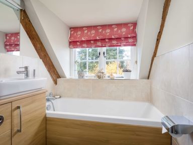 A bathroom with a bathtub a sink wooden cabinet and a window with red floral curtains at Courtyard House in Blockley