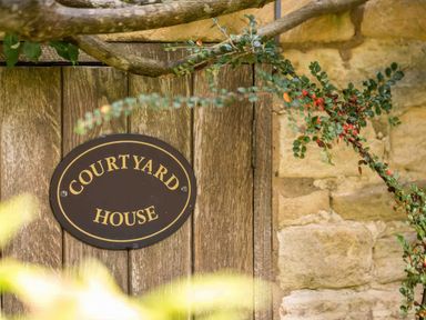 A wooden door with a Courtyard House sign surrounded by stone walls and foliage at Courtyard House in Blockley