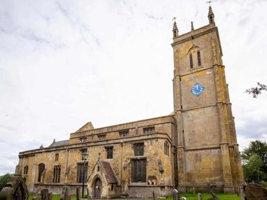An old stone church with a tall clock tower and arched entrance surrounded by gravestones