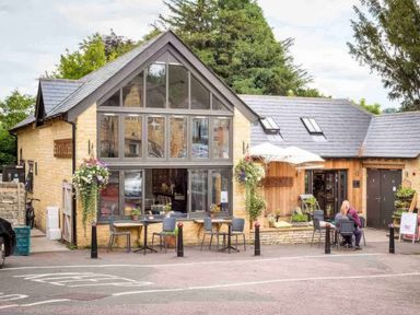 A small cafe building with outdoor tables and chairs and people sitting outside