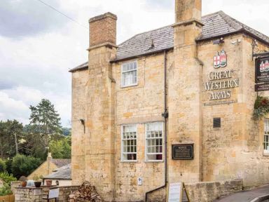 The exterior of a stone building with chimneys and windows showing the sign Great Western Arms at Courtyard House in Blockley