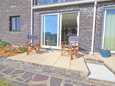 An outdoor patio area with two wooden chairs in front of sliding glass doors at Harbour Escape in Porthmadog