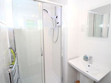 A bathroom with a glass-enclosed shower, a white sink with a faucet and soap, a wall-mounted mirror, and a towel rack at Harbour Escape in Porthmadog