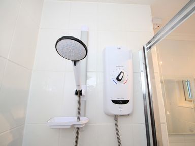 A white electric shower unit with temperature control and a detachable showerhead mounted on a tiled bathroom wall at Harbour Escape in Porthmadog
