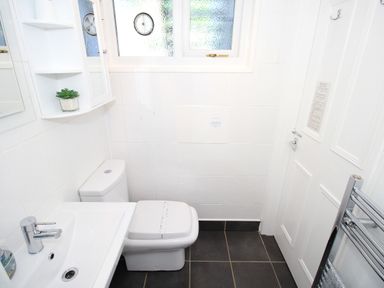 A small bathroom with a toilet, sink, wall cabinet with shelves, frosted window, and a radiator at Harbour Escape in Porthmadog