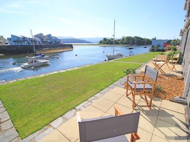 A patio with chairs and grass overlooking a river with boats at Harbour Escape in Porthmadog