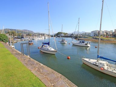 Sailboats moored in a marina with a stone wall and grass on the left at Harbour Escape in Porthmadog