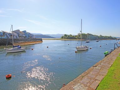 A river with sailboats moored alongside modern houses and a stone walkway at Harbour Escape in Porthmadog