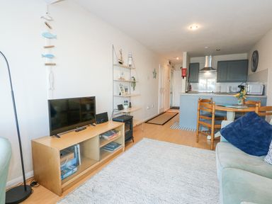 A living room with a sofa a TV on a wooden stand a dining table with chairs and a kitchen area at Harbour Escape in Porthmadog