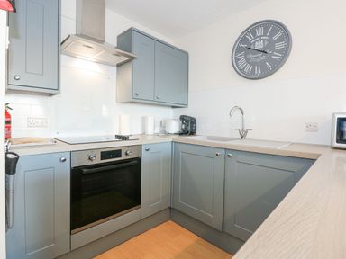 A kitchen with grey cabinets oven sink countertop and a wall clock at Harbour Escape in Porthmadog