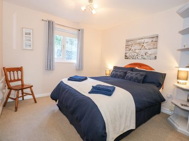 A bedroom with a double bed with blue and white bedding a wooden chair a window with curtains and a starfish wall art at Harbour Escape in Porthmadog