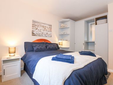 A bedroom with a double bed with blue bedding a white nightstand with a lamp and built in white wardrobes at Harbour Escape in Porthmadog
