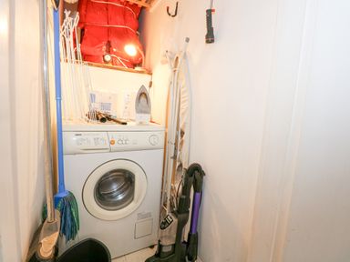 A laundry room with a washing machine mop broom ironing board and vacuum cleaner at Harbour Escape in Porthmadog