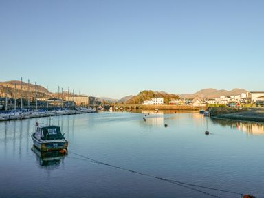 A body of water with boats docked along the sides and buildings in the background at Harbour Escape in Porthmadog