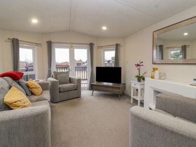 A living room with sofas a television on a stand and windows with curtains at Longdon Lodge in Wickhamford near Evesham