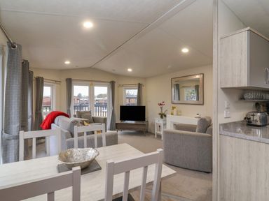 A living room with grey sofas a TV and a dining table with chairs at Longdon Lodge in Wickhamford near Evesham