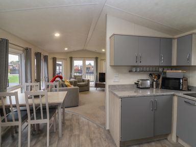 An open-plan kitchen and dining area with gray cabinets and a dining table with chairs next to a living room with armchairs and a television at Longdon Lodge in Wickhamford near Evesham