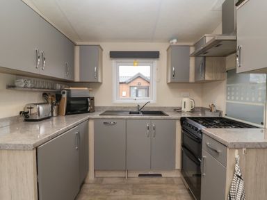 A kitchen with grey cabinets a black sink a window a toaster microwave kettle and a stove at Longdon Lodge in Wickhamford near Evesham
