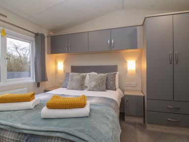 A bedroom with a bed with pillows and folded towels next to a window and gray cabinets at Longdon Lodge in Wickhamford near Evesham