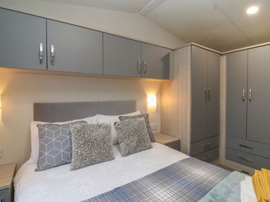 A bedroom with a bed, patterned pillows, overhead cabinets, and a wardrobe at Longdon Lodge in Wickhamford near Evesham