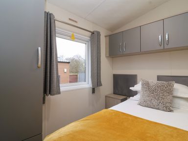 A bedroom with a bed covered by a yellow blanket and a patterned pillow and built in cabinets above the bed at Longdon Lodge in Wickhamford near Evesham