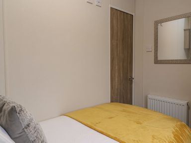 A bedroom with a bed covered in a yellow blanket two gray pillows a wooden door a radiator and a mirror on the wall at Longdon Lodge in Wickhamford near Evesham