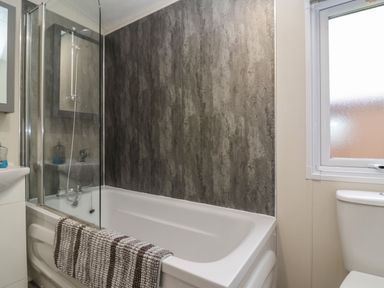 A bathroom with a bathtub shower combination a striped towel on the tub a toilet and a frosted window at Longdon Lodge in Wickhamford near Evesham